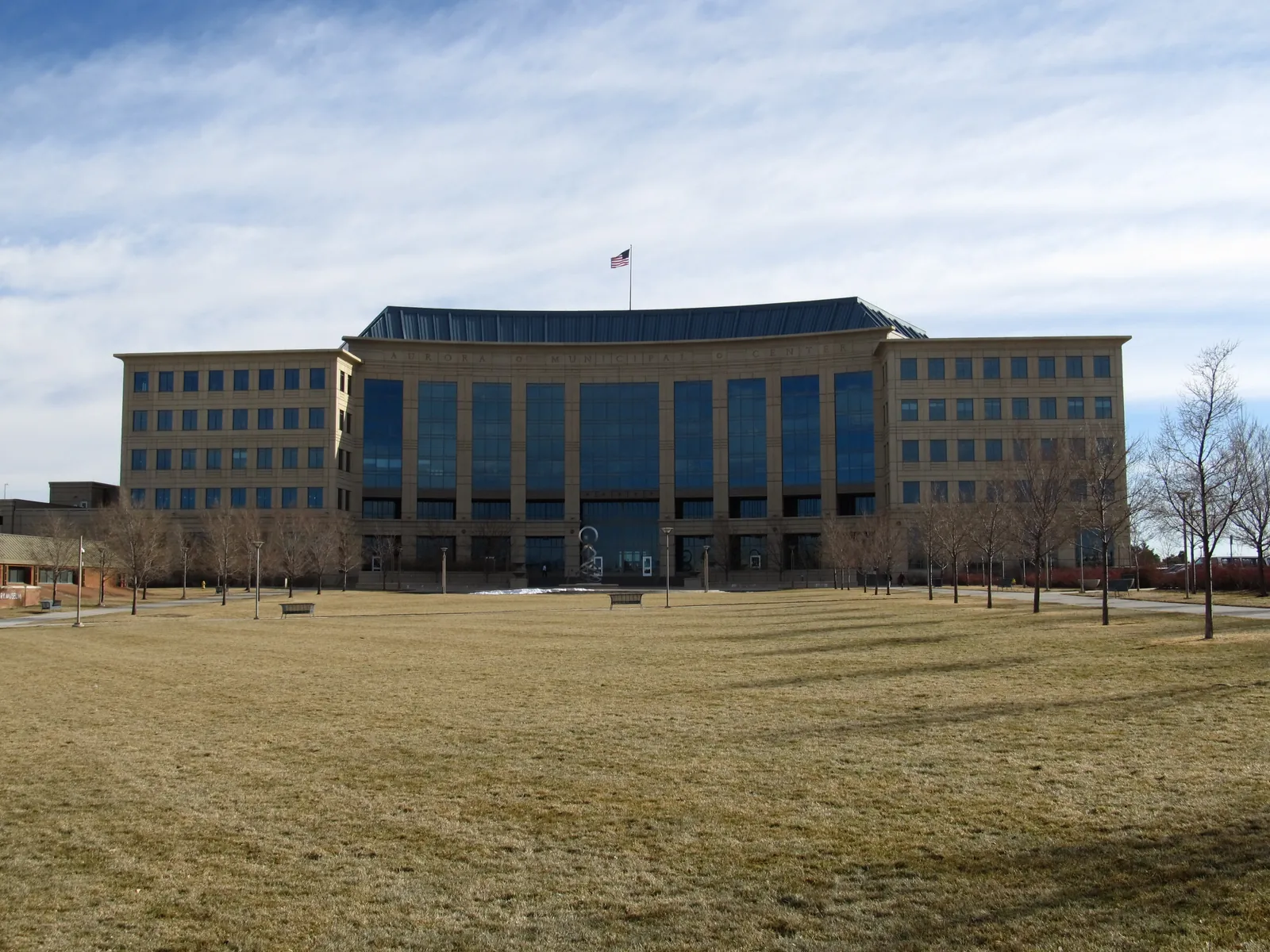 Aurora Municipal Center with its curved glass facade behind a dormant winter lawn and bare trees