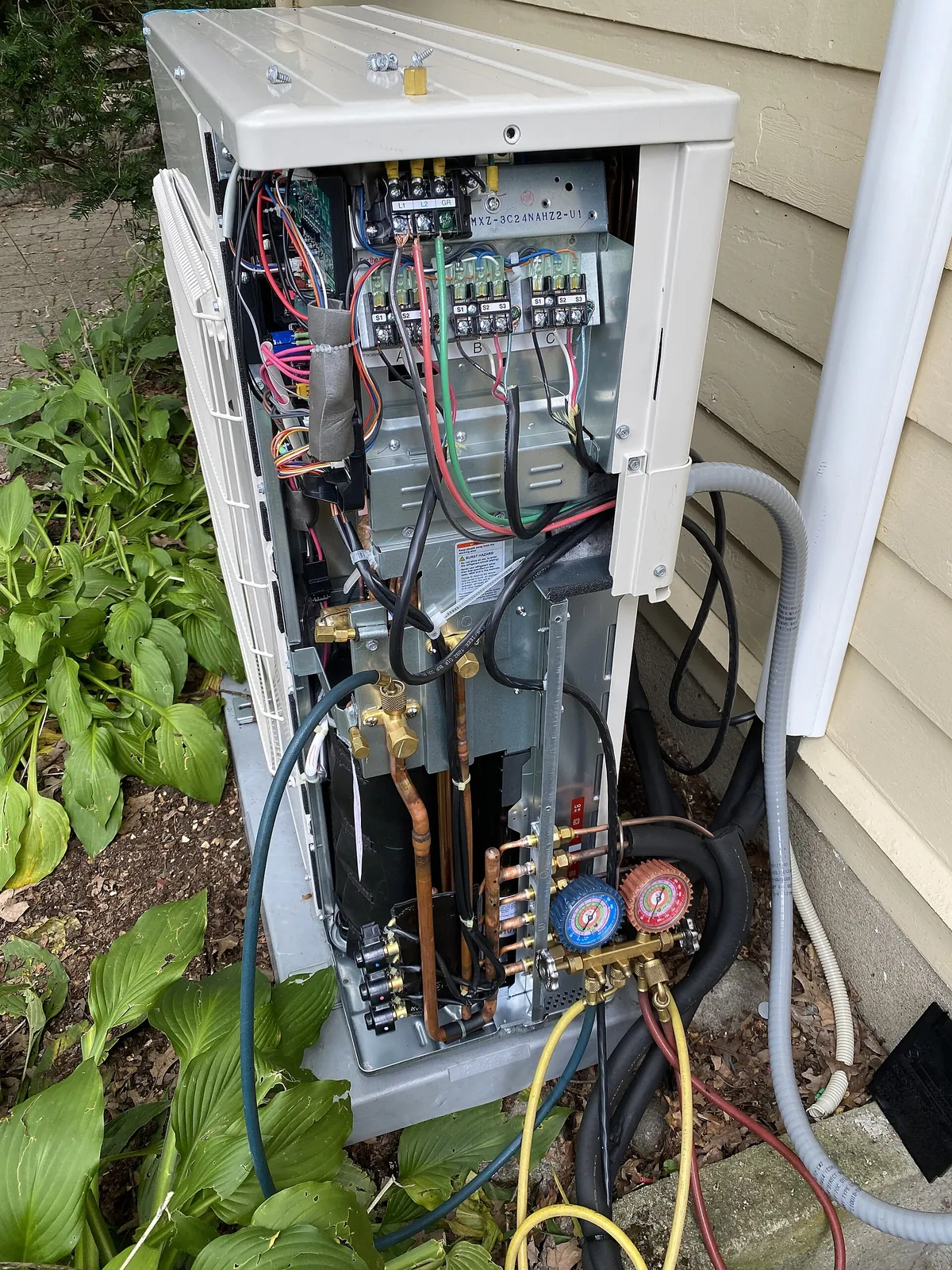 Heat pump outdoor unit with its service panel removed and refrigerant manifold gauges connected to the service valves