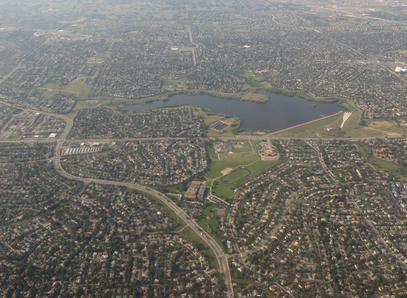 Aerial view of Quincy Reservoir and its dam surrounded by southeast Aurora neighborhoods, parks and curving streets
